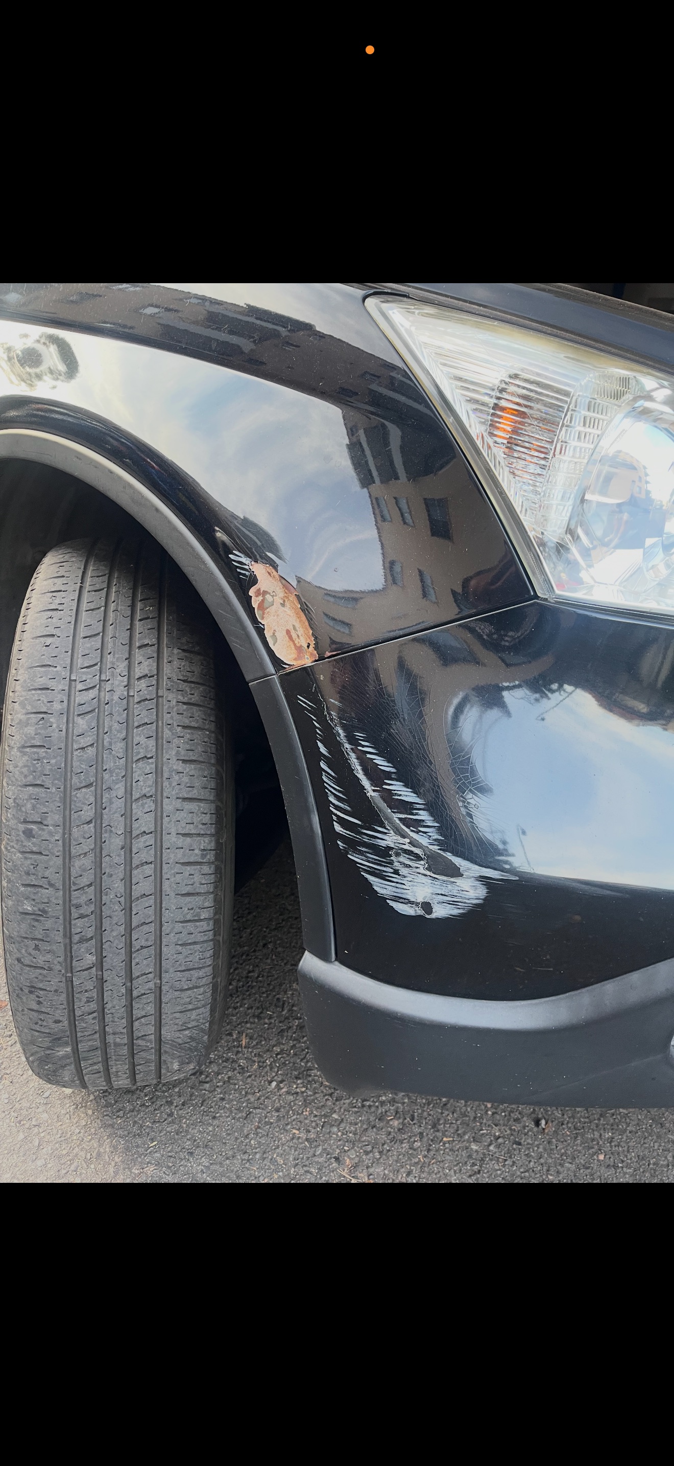 Black SUV front fender with paint chipped away and rust forming above the wheel arch — caught early before it eats the panel